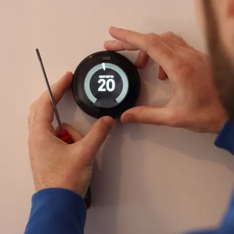 Main réglant un thermostat mural à 20 degrés